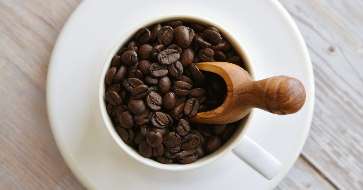 白いカップに入ったコーヒー豆と木製スプーン