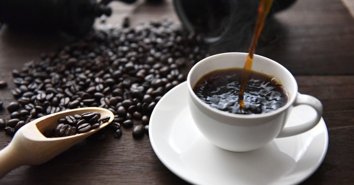 白いカップに注がれるコーヒーと広がる焙煎豆